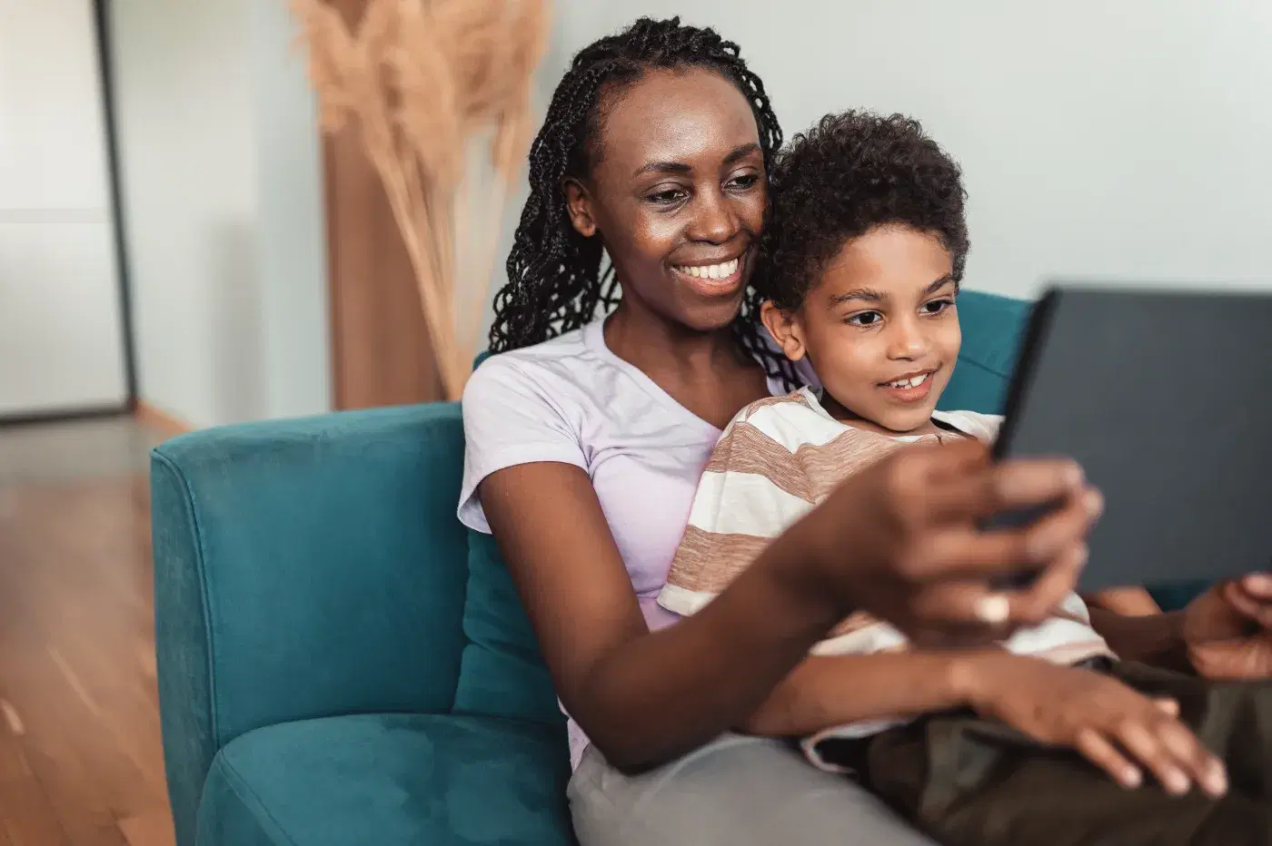 Mãe e filho no sofá de casa, olhando juntos a tela de um tablet