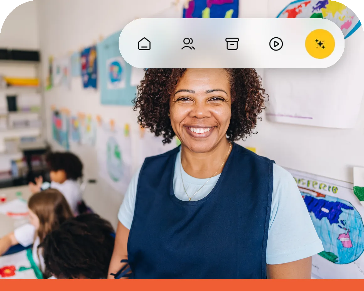 Professora sorrindo em uma sala de aula, com estudantes desenhando em uma mesa ao fundo